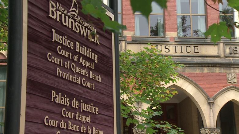 A sign for the Fredericton justice building appears in the foreground of the brick building itself.