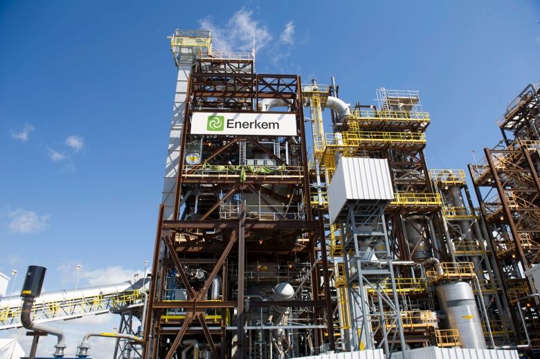 An industrial facility outdoors under a blue skies, showing pipes, walkways and stairways.