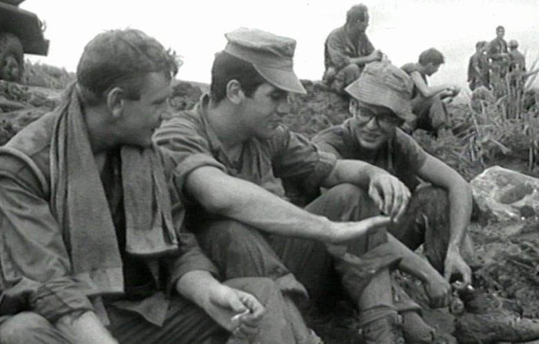 Picture of three men sitting close together on the ground, talking.