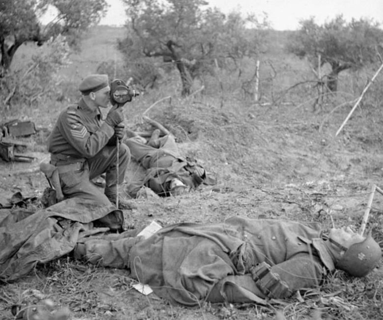 A black and white photo shows a Canadian military member positioned between two German bodies during the Italian Campaign of the Second World War.