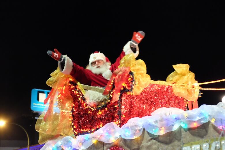 A man dressed as Santa Claus waves as he sits on a brightly coloured parade float.