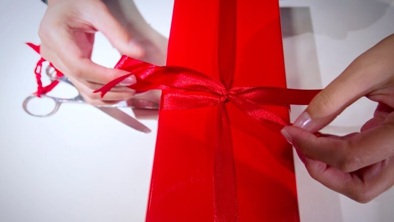 Two hands tying a red ribbon bow on a red rectangular box.