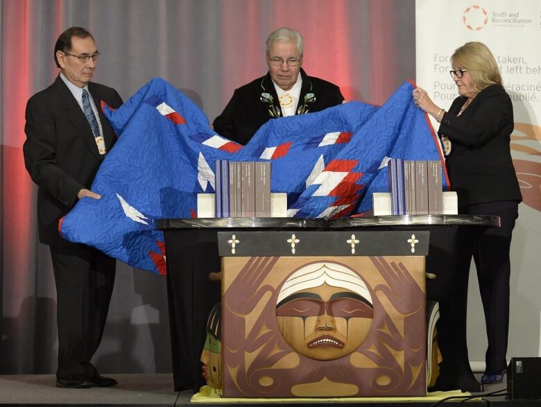 Three people remove a blanket to unveil a series of reports 