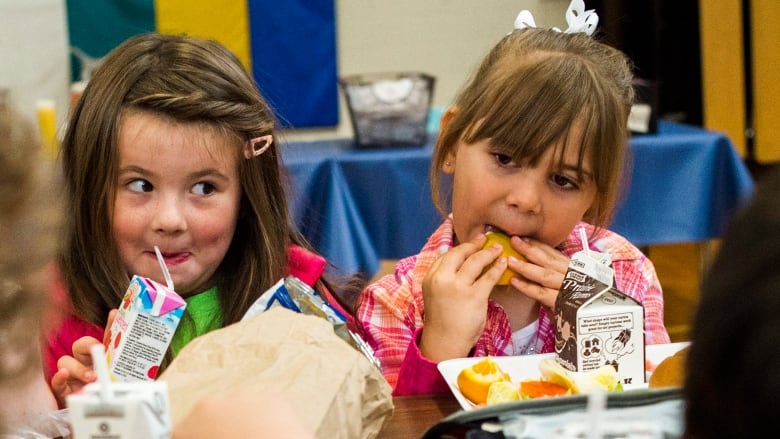 Two young girls smile as they eat a lunch and drink from juice boxes.