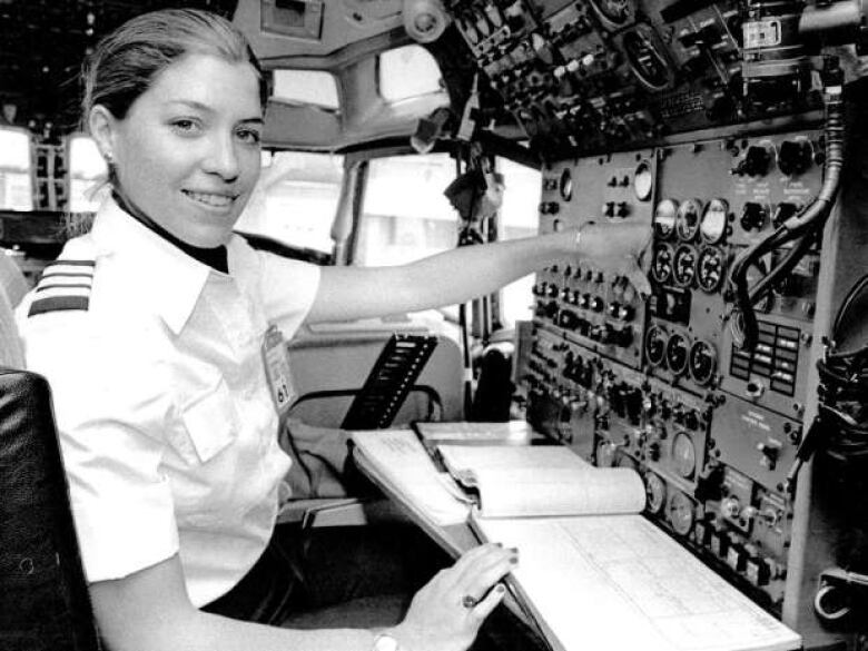 A woman sits at the controls to a flight in a black-and-white photo.