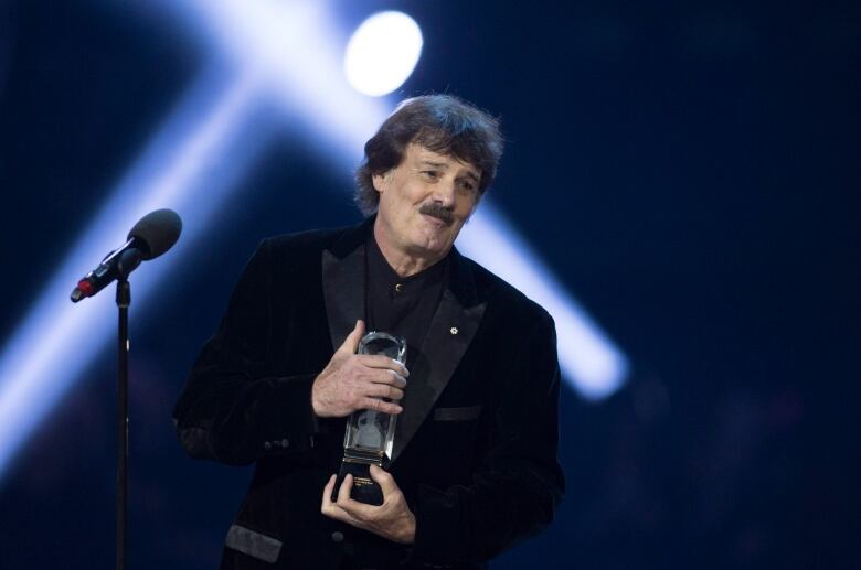 A man smiles as he stands on a stage, holding an award.