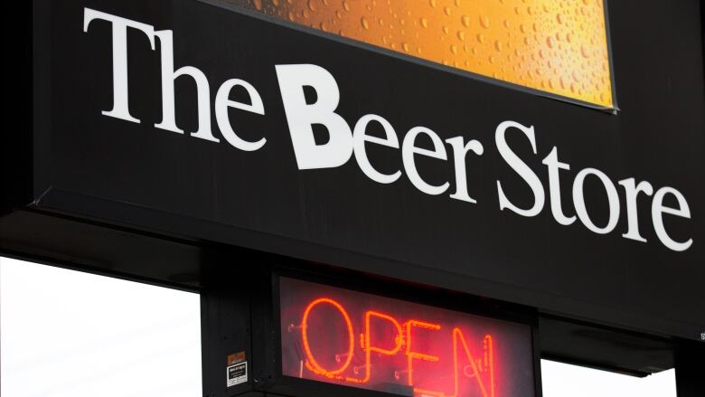 A large sign outdoors on a cloudy day, close up, reads The Beer Store in white text against a black background, with a red neon 