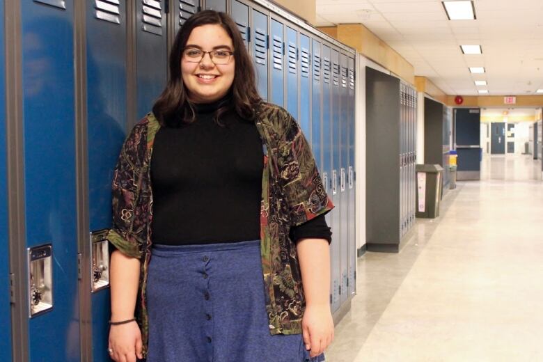 A woman stands in front of a row of lockers and smiles. 