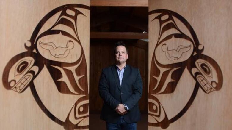 A man in a dark suit jacket stands between two panels featuring Indigenous designs.