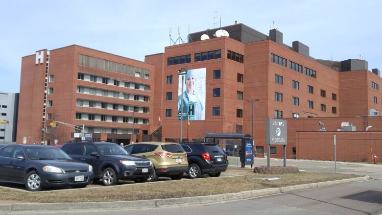 A large red brick building with a large letter 'H' on it, as well as a large image of a health-care provider wearing medical scrubs.