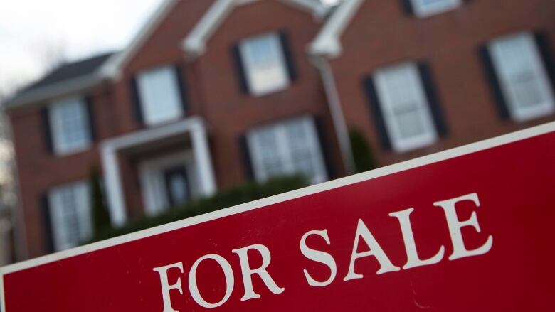 A red for-sale sign in front of a red brick home.