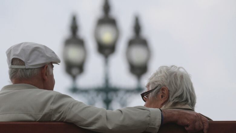 Two seniors sit on a bench with their backs turned.