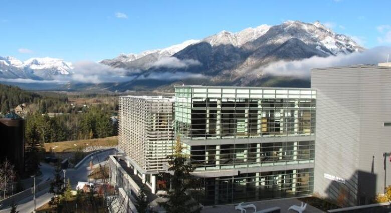 A large glass building is seen with trees, mountains and clouds in the background.