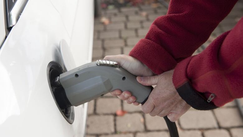 Two hands can be seen putting an electric charger into the side of a white car.