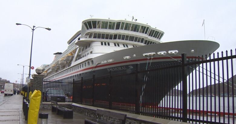 A large ship is docked at a waterfront. In the foreground is a large metal fence. 