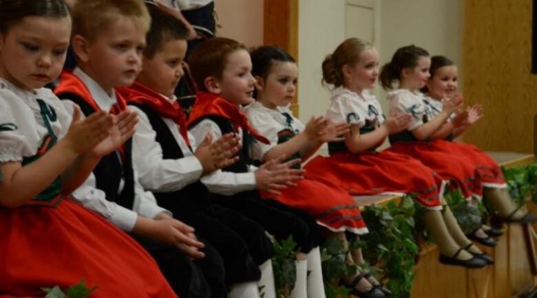 Children sitting in suits and dresses and clapping.