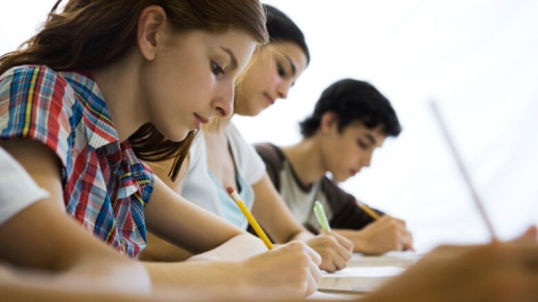 A close up of students writing exams at desks 