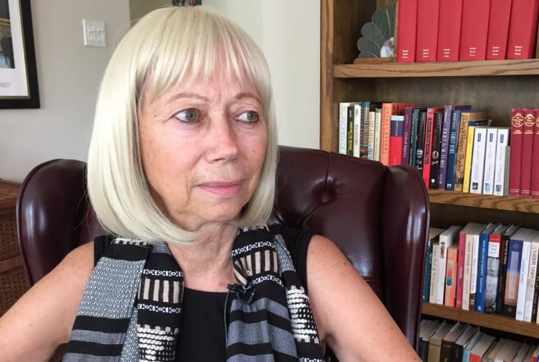 A woman sits in an office in front of a bookshelf.