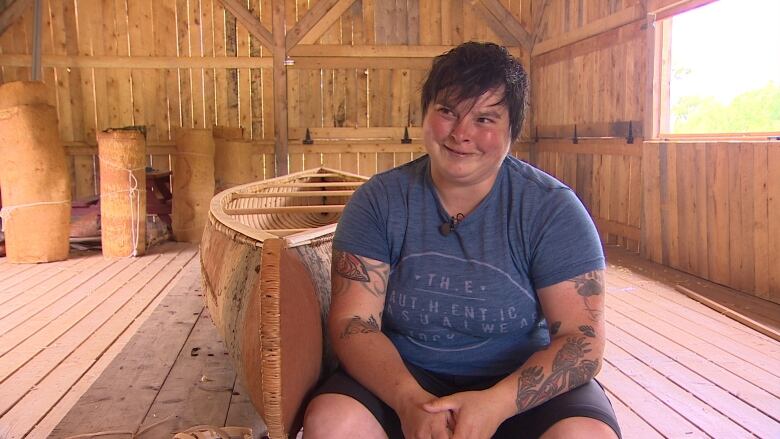 a woman sits in front of a birch bark canoe. 