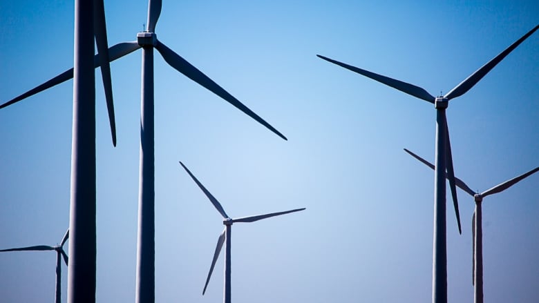 Six wind turbines are seen against the backdrop of a clear blue sky. 