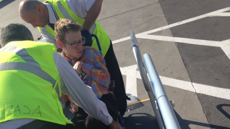 A man is wheeled up a ramp into an airplane by staff.