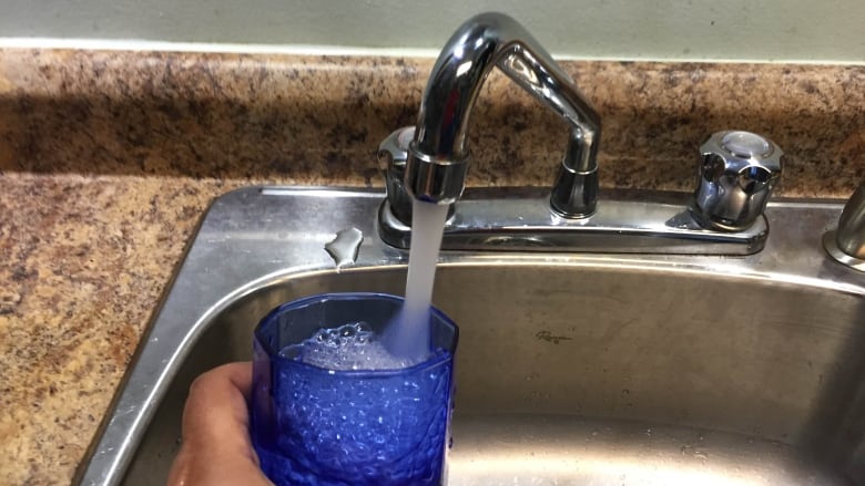 A tap fills up a cup of water in a sink.