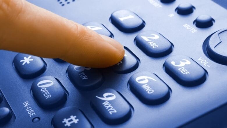 A finger is touching the keypad of a phone.