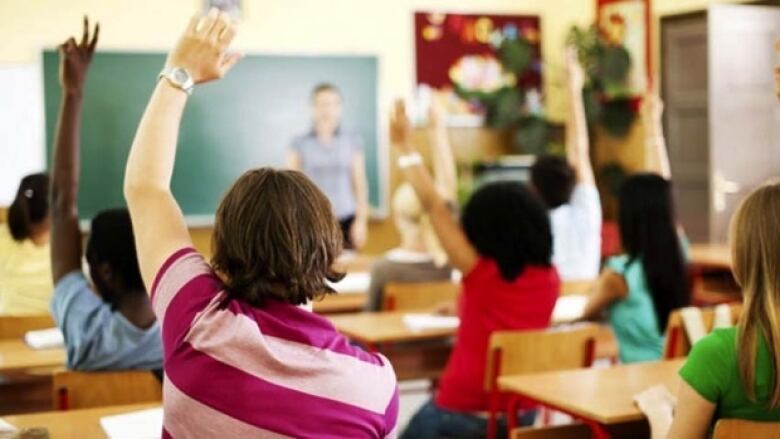 Group of students in classroom raise their hands. 