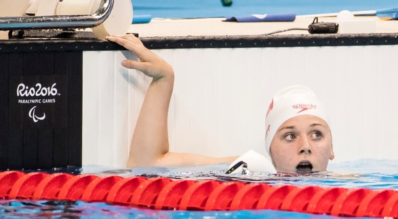 A swimmer in a white cap pokes her head out of the water. The pool she is in is labeled 