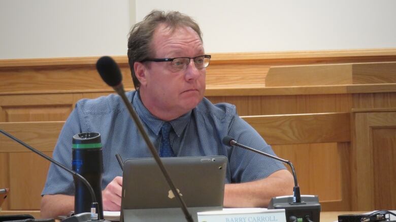 A white man sits in a council chamber.