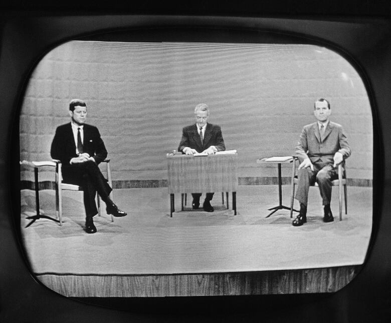 Black and white photo of TV studio with Kennedy on one side, Nixon on the other.