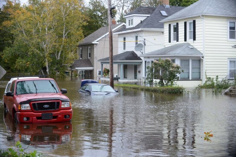 Vehicles are seen submerged in water on a flooded residential street.