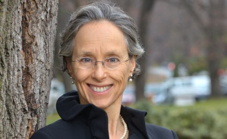 A woman stands next to a tree and smiles for a portrait.