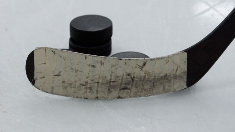 A hockey stick and pucks are seen up close on ice