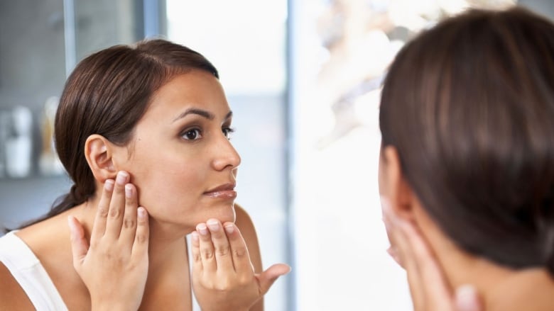 A woman stares at her face in a mirror.