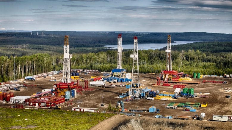 An aerial view of a drilling operation with forests and a lake in the distance.