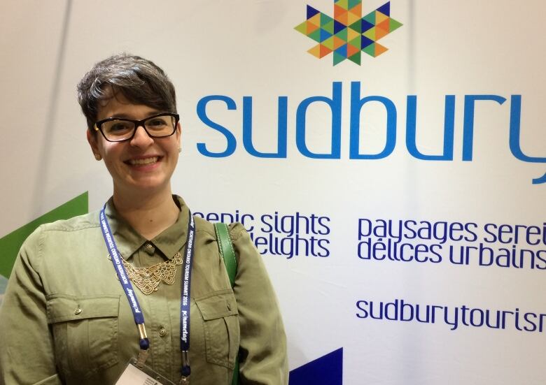 A woman stands in front of a Sudbury banner.