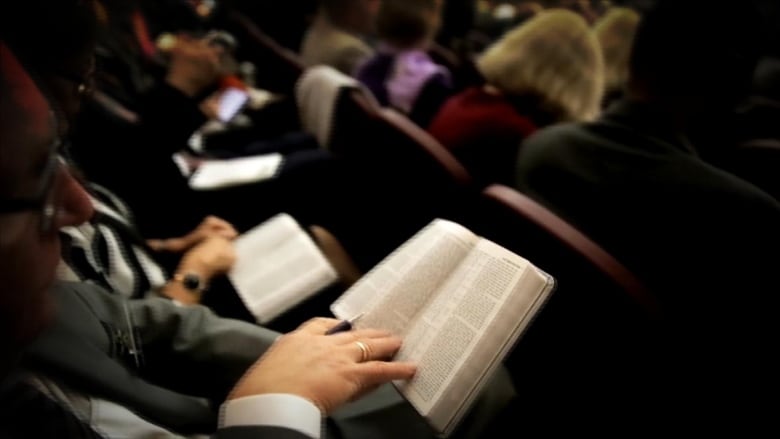 A scene from a Jehovah's Witness congregation shows people sitting in rows, reading from Bibles.