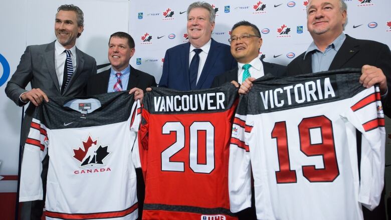 Five men are pictured standing holding up sports jerseys. 