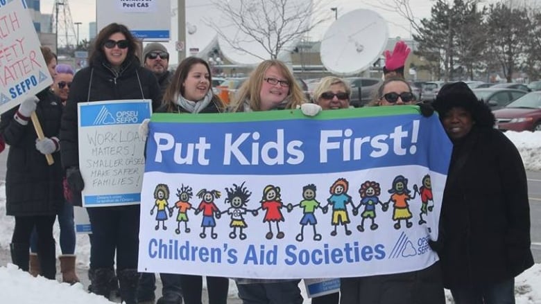 A group of people hold up a banner that says Put Kids First Children's Aid Societies.