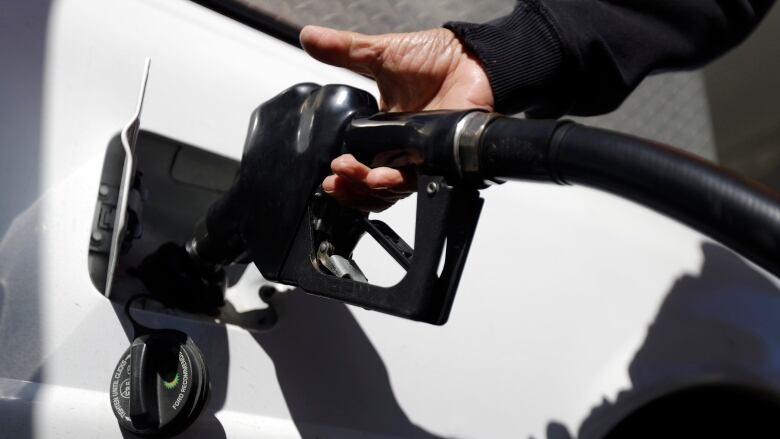 A closeup of a person holding a fuel pump nozzle in the gas tank of a white truck.