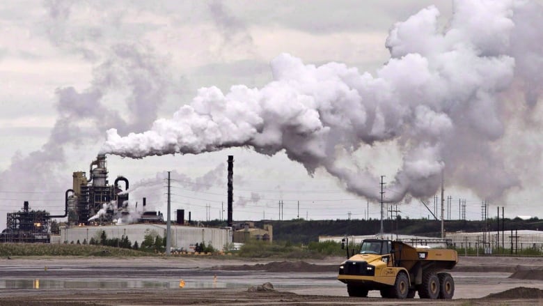 A construction truck is pictured in front of a smokestack.