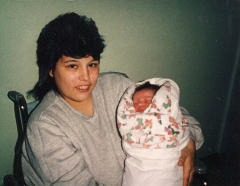 A woman sits in a chair holding a small child. 