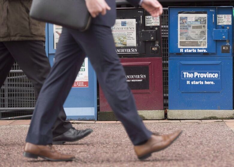 A man walks past newspaper boxes containing the Vancouver Sun and the Province in downtown Vancouver.