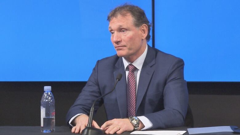 Man in a suit and tie sits in front of a microphone