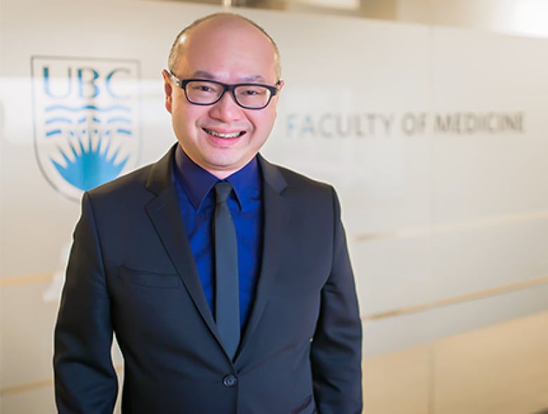 Man smiling and wearing a blue suit and tie in front of a UBC Faculty of Medicine sign.