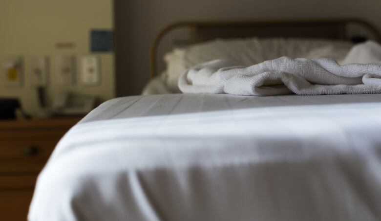 A bed can be seen with white sheets and a white blanket on top.