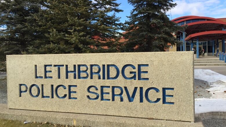 A sign reading Lethbridge Police Service sits on the grass in front of a building. 