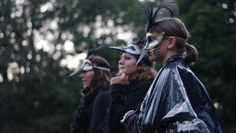 Three women are dressed in black and crow masks.