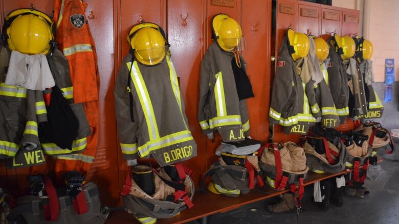 Firefighter helmets, coats and boats hang in a row on some orange lockers in a fire hall